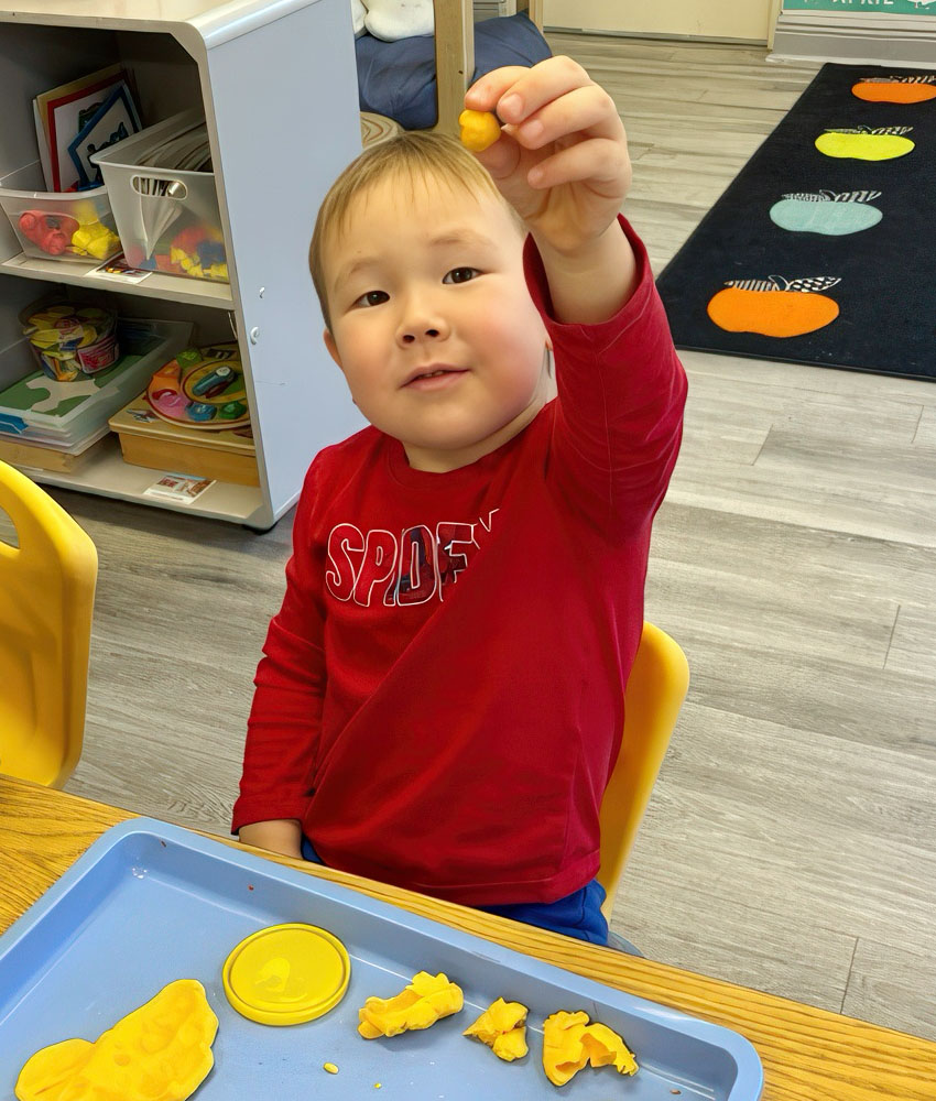 A young boy is smiling while holding a piece of yellow playdoh , capturing a moment of happiness and curiosity